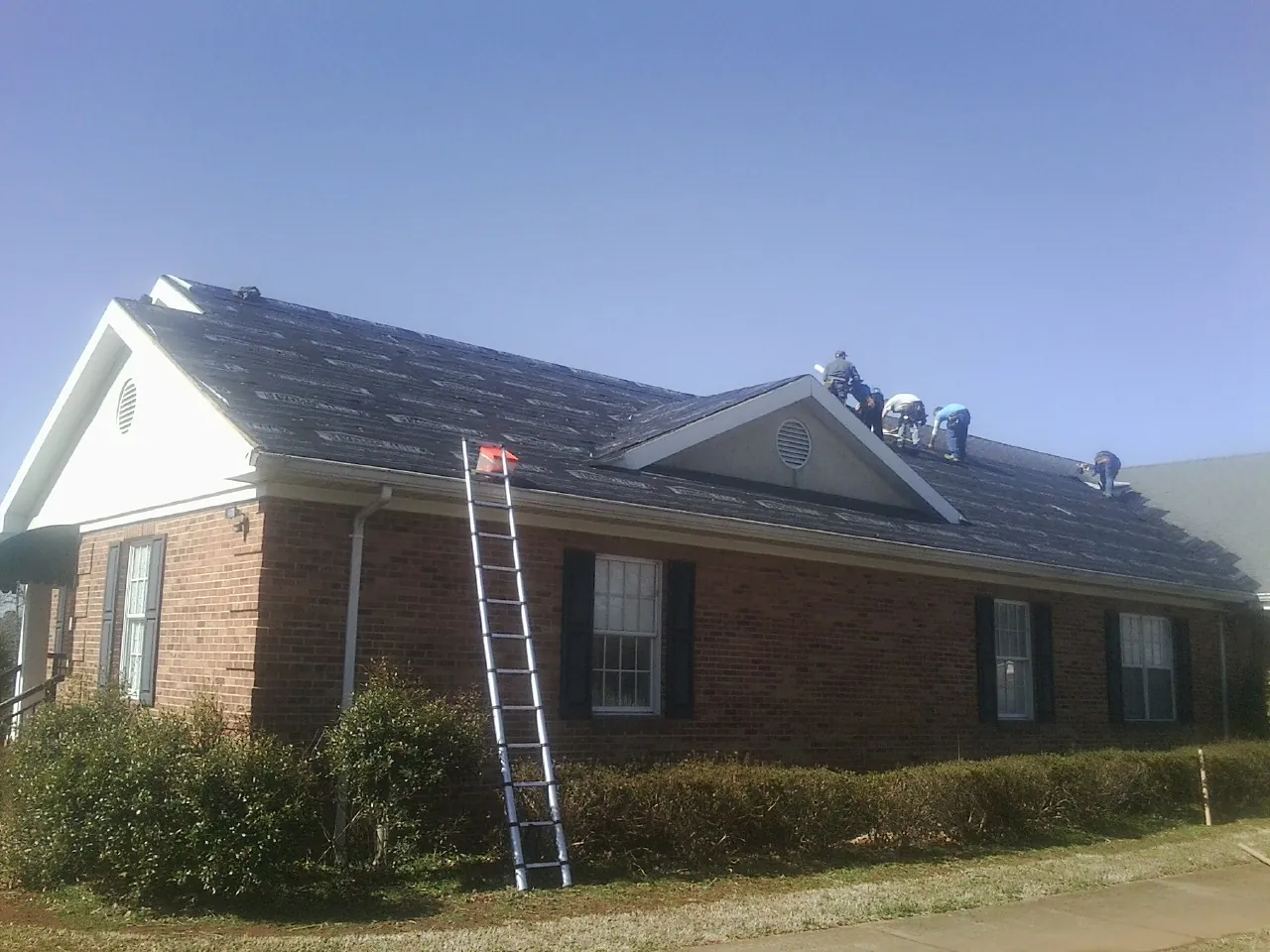 Crew tearing shingles off a brick ranch roof with a ladder set — Metal Roof Repair work by our crew in Hackettstown