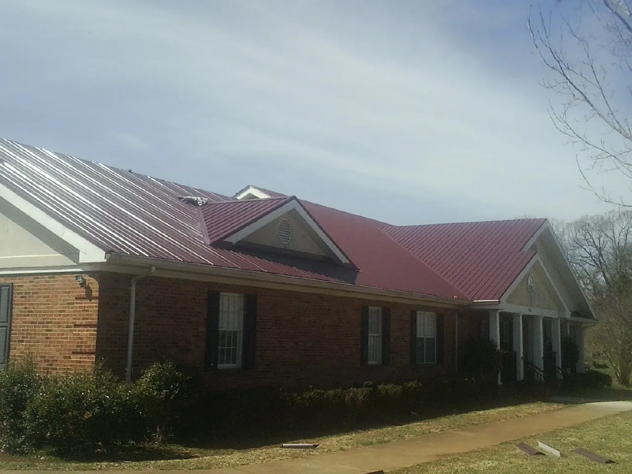 Red metal roof with gabled entries on a long brick building, from a Hail Damage Roof Repair job in Hackettstown