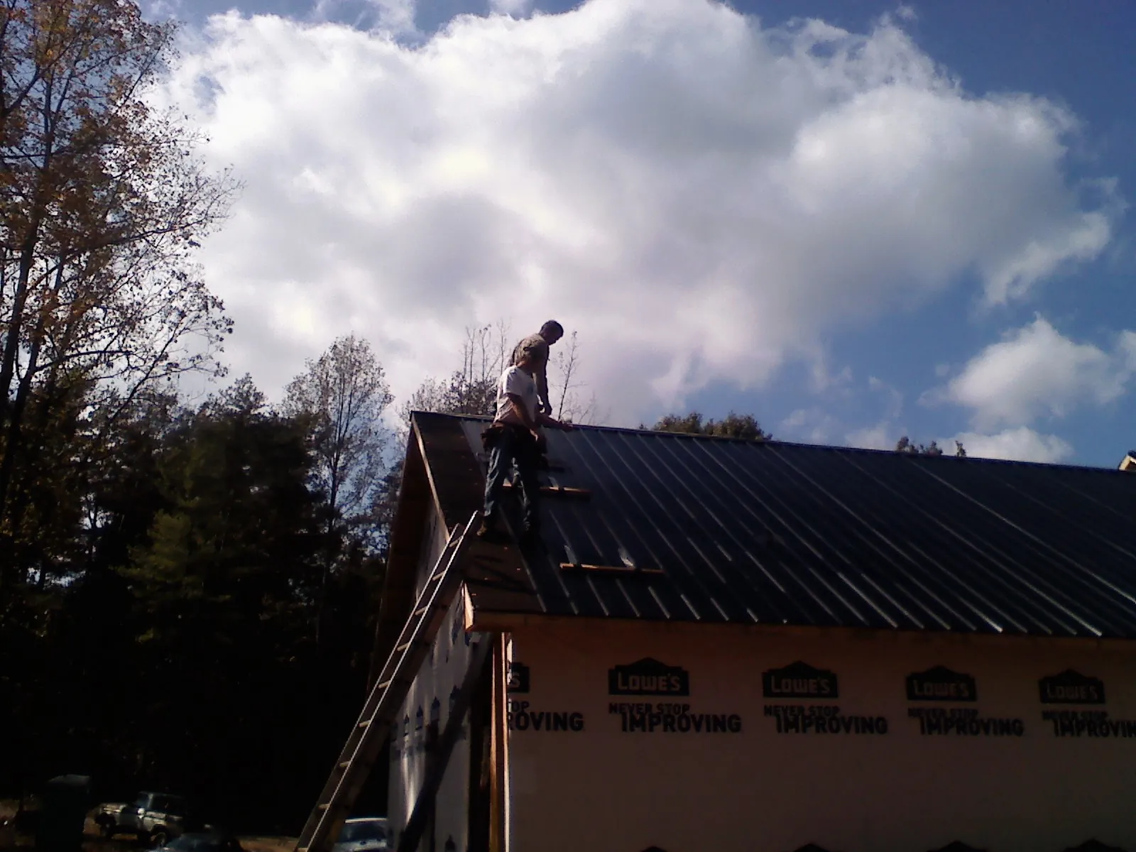 Roofer fastening dark metal panels high against a cloudy sky, from a Roof Inspection job in Hackettstown